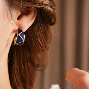 Close-up of vintage wide C-shaped earrings with blue and gold enamel geometric patterns