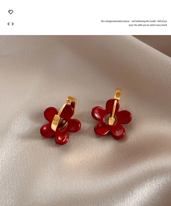 Détail de boucles d'oreilles fleur en émail rouge sur soie champagne avec attaches dorées