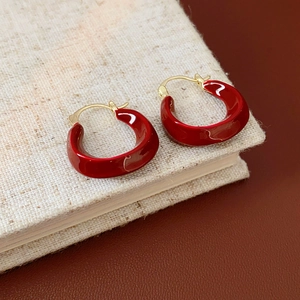 Detail of red enamel U-shaped gold earrings placed on a beige linen book cover