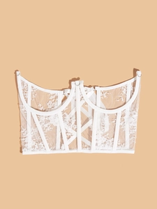 Detail view of a white lace corset top with sheer mesh panels and delicate ribbon bow