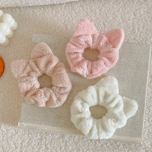 Detailed plush cat ear scrunchies in pink, apricot, and white on a textured book