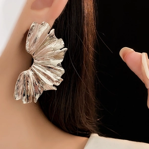 Macro shot of silver fan-shaped leaf earring with textured pleats on female model