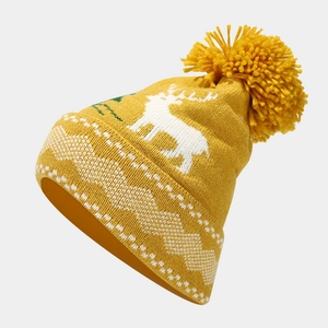 Close-up of yellow knit hat featuring white reindeer jacquard pattern and soft pom-pom
