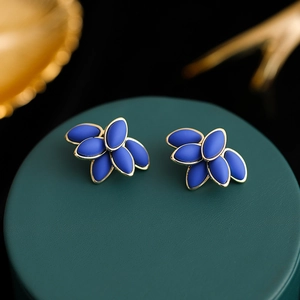 Macro detail of elegant gold-rimmed blue petal earrings on a dark green display stand