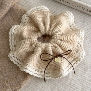 Detail of beige knitted scrunchie with brown bow and engraved gold believe pendant