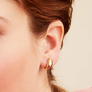 Close-up of polished 18K gold teardrop earrings worn on ear showing glossy finish