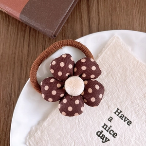 Detailed shot of brown floral hair tie with beige plush center on a white plate