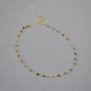 Close-up of a minimalist gold necklace featuring colorful natural stone beads and lobster clasp