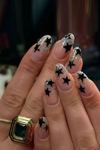 Close-up of almond-shaped press-on nails with black stars and silver glitter decor