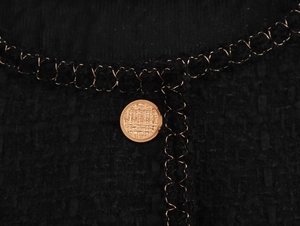 Dettaglio dell'abito in tweed nero con bottoni metallici dorati e piping testurizzato