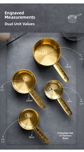 Set of four gold stainless steel measuring cups on a dark stone baking surface