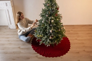 Detail of deep red knitted Christmas tree skirt with wavy scalloped edges on floor