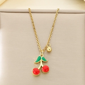 Close-up of golden necklace featuring red and green enamel cherry pendant on beige surface