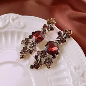 Vintage leaf earrings with deep red square gemstones and bronzed crystals on a ceramic plate