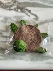 Detail of a handmade crochet turtle coaster in green and brown wool on marble surface
