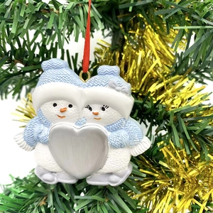 Close-up of resin snowman couple ornament with silver heart hanging on a Christmas tree