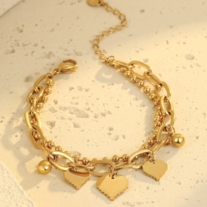 Detalle de pulsera dorada de varias capas con colgante de corazón y pequeña bola