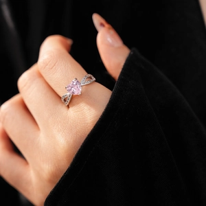 Close-up of a silver ring with a pink heart-shaped diamond worn on a model's finger