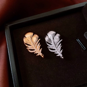 Detailed close-up of 18k gold and silver feather brooches with zircon micro-pave inlay