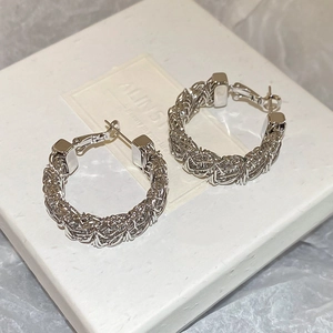 Detailed view of silver woven wire hoop earrings on a textured gift box background