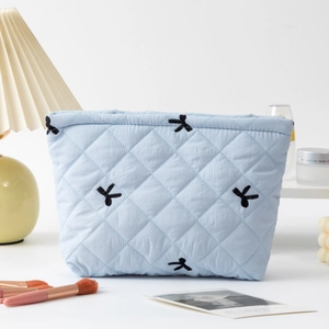 Detail of light blue quilted cosmetic bag with black ribbon embroidery in home setting
