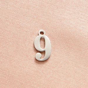 Detailed macro view of silver number nine stainless steel pendant on textured fabric