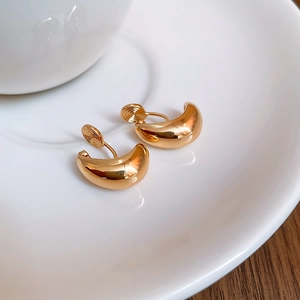 Dettaglio di orecchini a clip a goccia dorati lucidi su un piatto bianco elegante