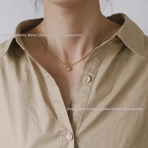 Detail of a dainty 18K gold plated bead chain with a round green bead pendant on a model
