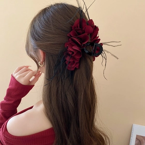 Detail view of burgundy chiffon flower hair claw with black feather accents on model