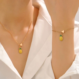 Dettaglio del set di gioielli dorati con ciondolo ananas smaltato e piccolo charm a cuore