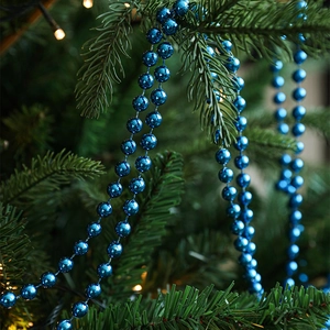 Glossy metallic blue bead garland draped on a Christmas tree with warm glowing lights