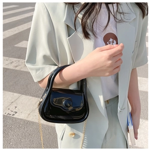 Detail of black glossy mini bag with gold chain strap on a street style model