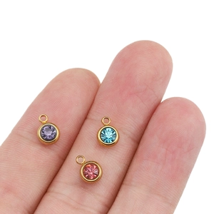 6mm gold-plated stainless steel birthstone charms in purple, blue, and pink held on fingertips