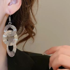Close-up of tiered silver circular hollow hoop earrings worn by a model in soft lighting