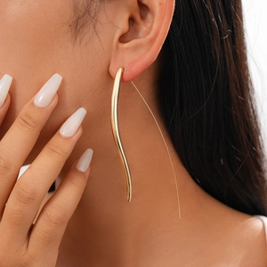 Detail showing long wavy golden metal drop earrings on model for a sleek minimalist look