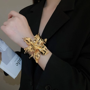 Detail of a large gold metal flower cuff bracelet with a polished wavy petal texture