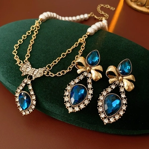 Detail of vintage jewelry set with blue teardrop stones, pearls and bow on green velvet