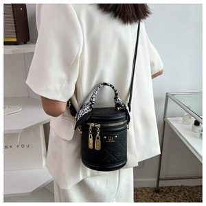 Detail of black cylindrical bucket bag with embossed pattern and silk scarf handle decoration