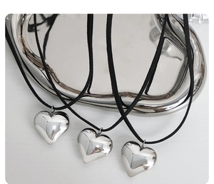 Close-up of three polished heart pendants on black cords over a silver tray