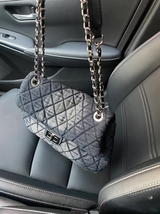Detail of dark grey denim quilted bag with silver chain strap on a black leather seat