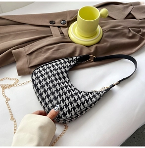 Detail of houndstooth crescent bag with black leather strap and gold chain decoration