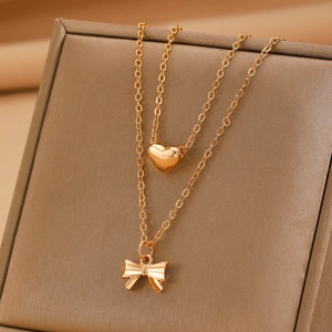 Macro shot of double-layer gold necklace featuring a heart pendant and bow charm detail