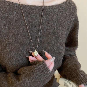 Detailed close-up of golden oval textured pendant on a brown cord with knit sweater