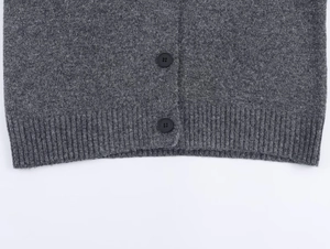 Macro detail of dark grey knit cardigan featuring black buttons and ribbed hem texture