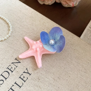 Close-up of a seaside acrylic starfish with fabric flower and pearl on a duckbill hair clip