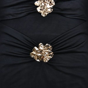 Detalle de botones de flores de metal dorado en la tela plisada negra de un vestido