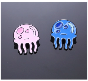 Detailed view of pink and blue jellyfish enamel pins on a dark reflective surface
