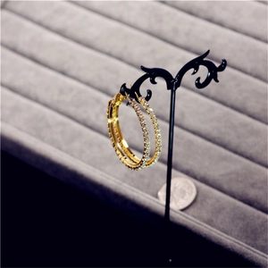 Detailed view of oversized gold hoop earrings with crystals next to a coin for scale