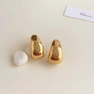 Detailed close-up of high-polish gold teardrop earrings on a soft neutral background