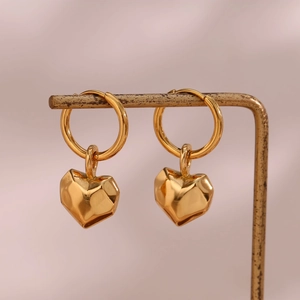 Detail of gold heart earrings with irregular faceted design on a metal display stand
